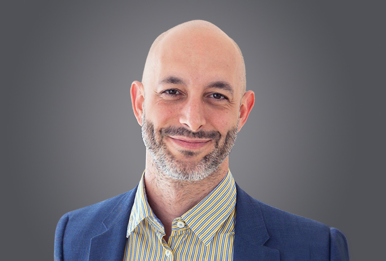 Smiling bald man with a short beard in a blue blazer and striped shirt, looking at the camera.