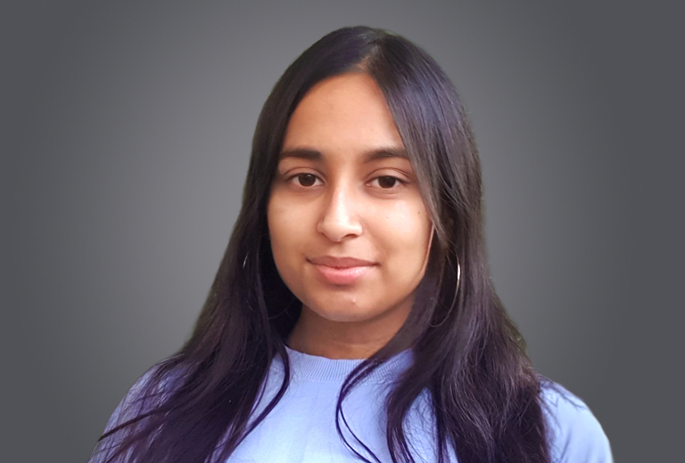 Young woman with long dark hair and hoop earrings, wearing a light purple sweater, against a gray gradient background.