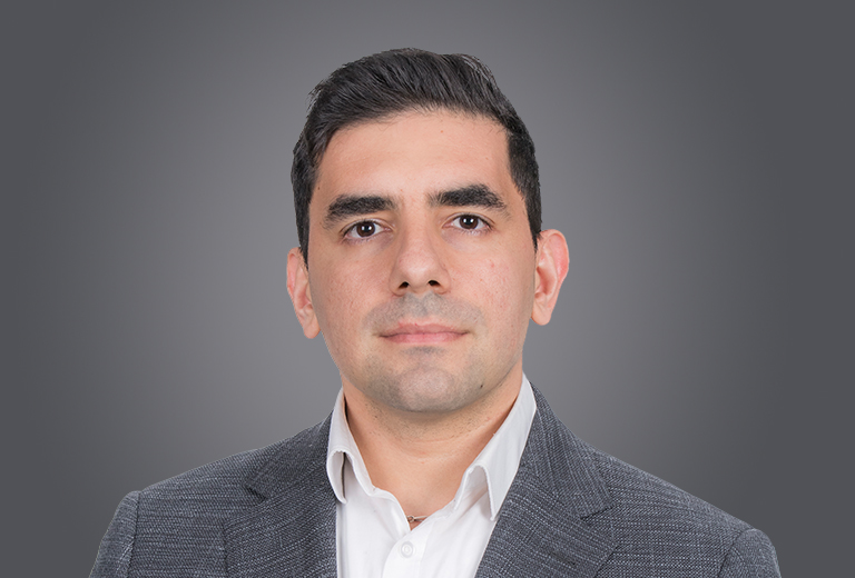 Professional head-and-shoulders portrait of a man in a gray blazer and white dress shirt against a neutral gray backdrop.