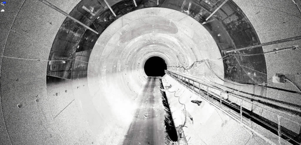 A detailed, black and white 3D point cloud scan from inside a large tunnel, showcasing digital technology in tunnel construction.
