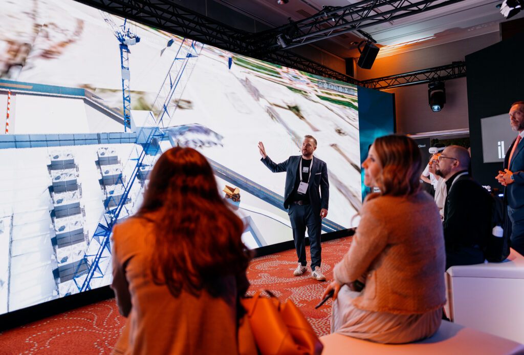 Markus Sauerbeck demonstrating a 4D construction simulation on a large, immersive screen to an audience at a Bentley technology showcase.