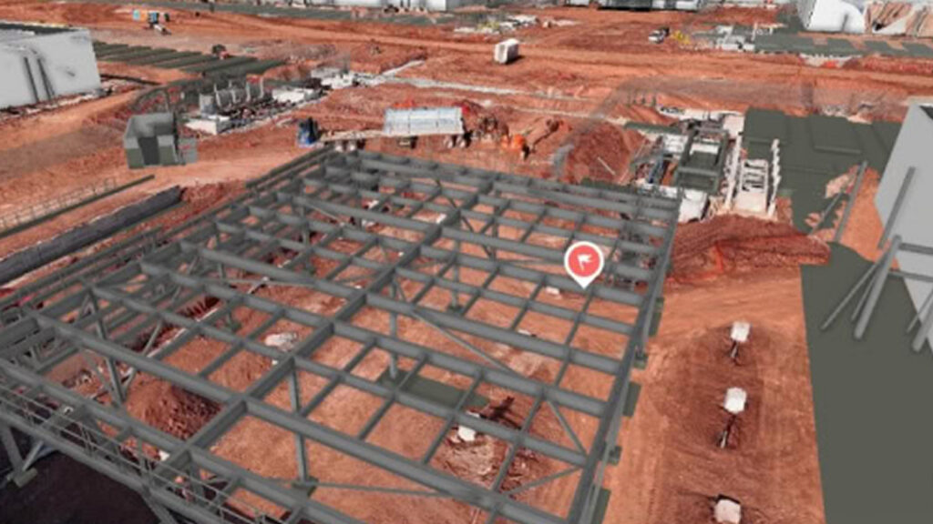 Active construction site with a steel frame structure on red dirt, workers and equipment in the background.