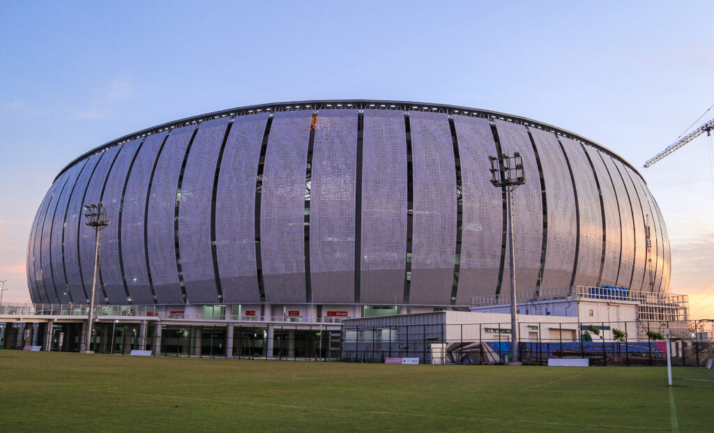 An external view of the massive, modern Jakarta International Stadium at dusk, showcasing its distinctive perforated facade, a finalist project by Buro Happold.