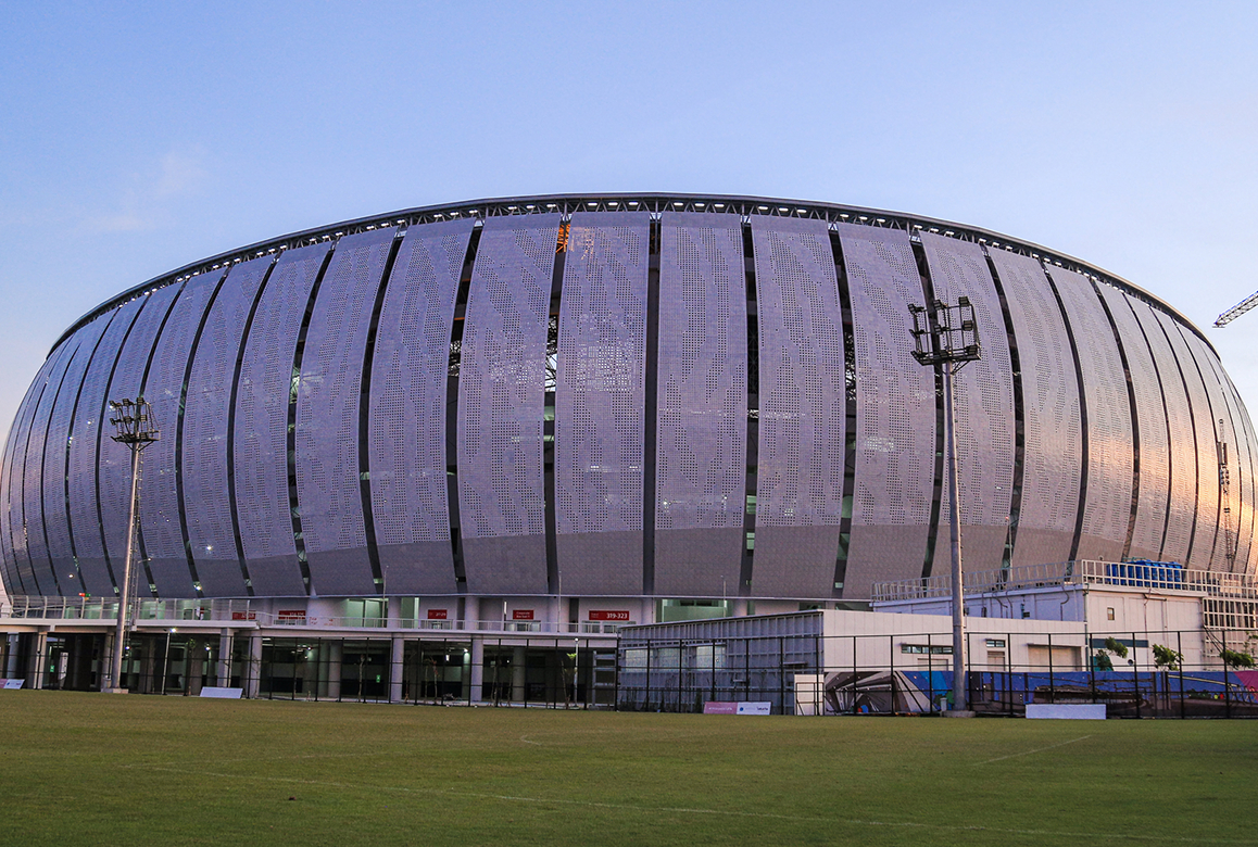 An external view of the massive, modern Jakarta International Stadium at dusk, showcasing its distinctive perforated facade, a finalist project by Buro Happold.
