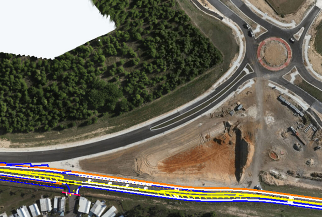 Aerial view of a road construction site with a roundabout and new asphalt paving, adjacent to a forested area.