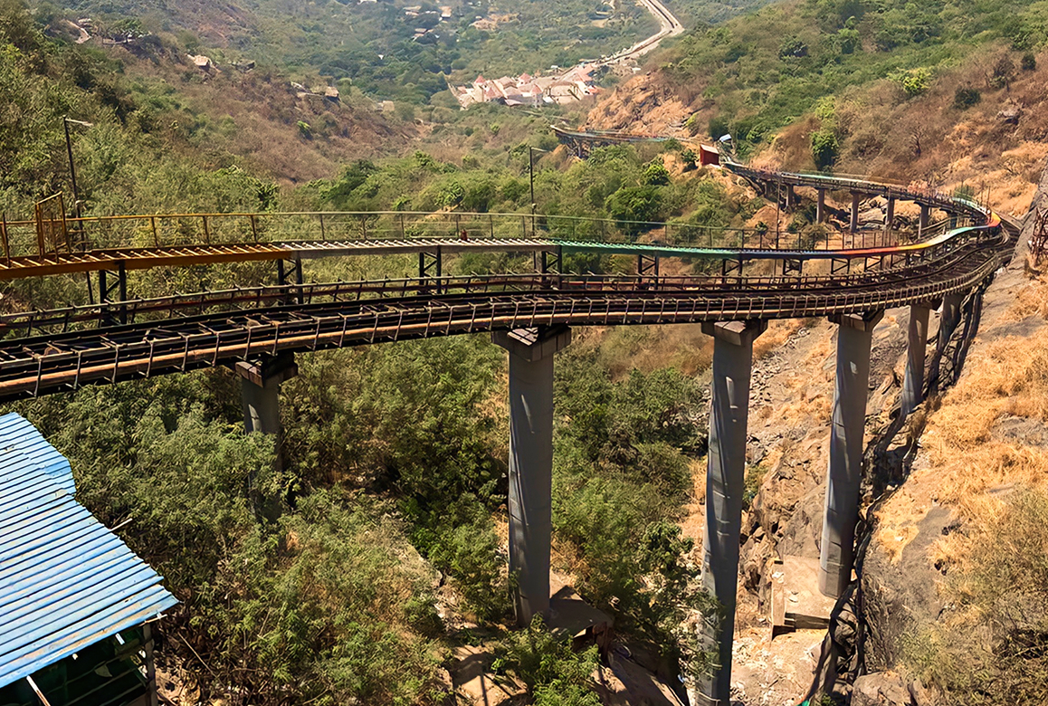 Winding elevated railway viaduct stretching across a valley with green hills and a distant village.