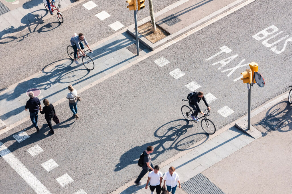 Aerial view of cyclists and pedestrians crossing a city intersection with marked bus and taxi lanes.