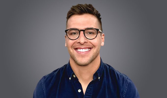Ben Townsend, a man with short brown hair, glasses, and a dark blue button-up shirt, smiles in front of a plain gray background.