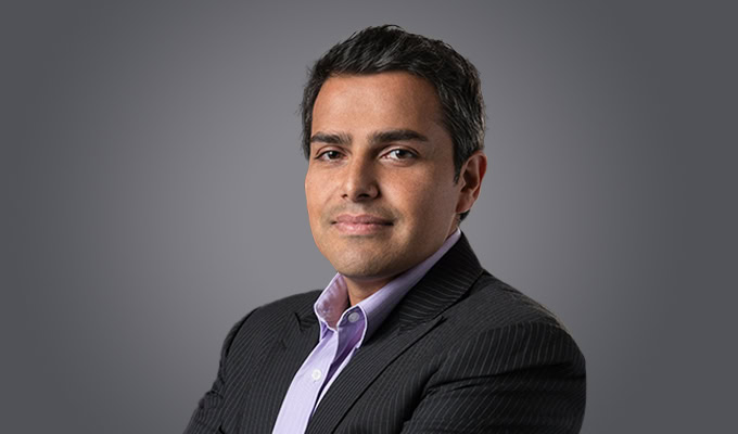 A man, identified as Bibhuti Aryal, in a dark striped suit and light purple shirt poses with arms crossed against a plain grey background.