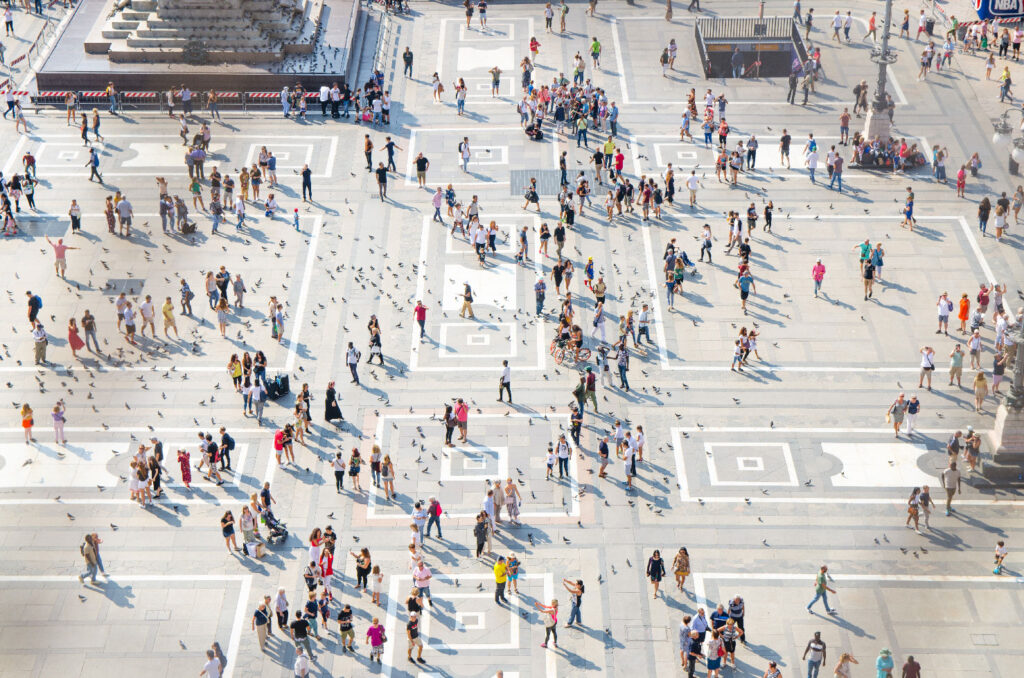 Aerial view of a large open square with scattered groups of people walking and gathering; geometric patterns decorate the ground.