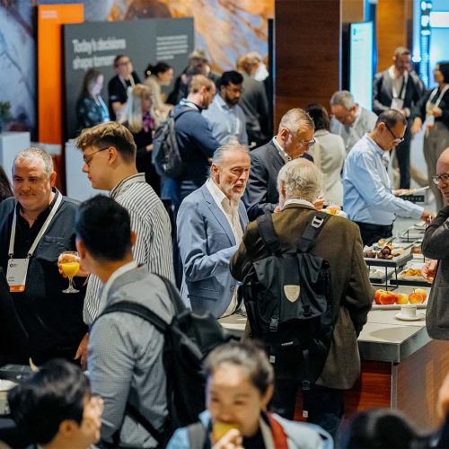 Business professionals mingle at a conference buffet, sampling snacks and drinks at a crowded expo.