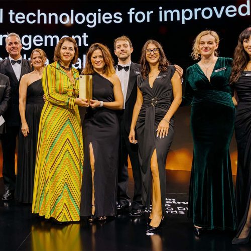 A group of ten people stands on stage in formal attire, some holding a trophy, in front of a screen displaying text about digital technologies for improved management.