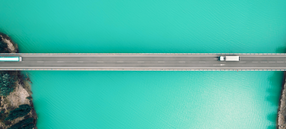 A truck drives across a straight bridge over vibrant turquoise water, the scene unfolding like a precisely planned agenda when viewed from above.