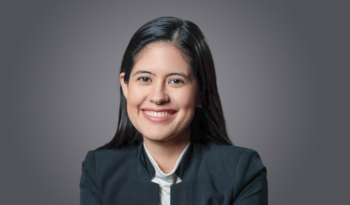 A woman with long dark hair, wearing a dark blazer and white top, smiles at the camera against a plain grey background—capturing the professional style associated with Richard Vestner.