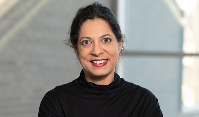 Person with dark hair tied back, wearing a black turtleneck, smiling at the camera with a neutral blurred background.