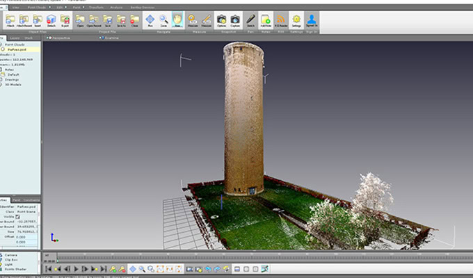 A 3D modeling software interface displaying a digital model of a tall cylindrical tower on a grassy area with surrounding trees and a fence.