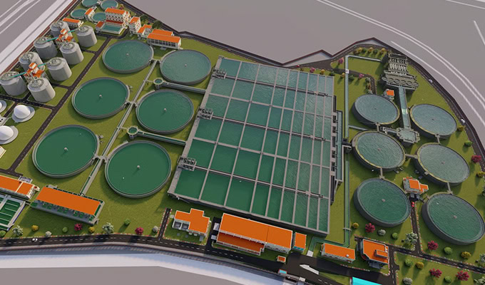 Aerial view of a large water treatment plant with multiple circular and rectangular tanks, buildings with orange roofs, and surrounding roads.