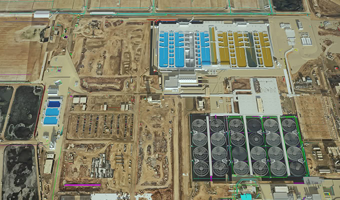 Aerial view of an industrial facility with multiple rectangular buildings, circular storage tanks, and dirt roads surrounding the site.