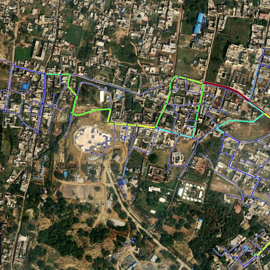 A satellite view of an urban area in emerging economies with roads highlighted in green, yellow, red, and blue lines over various buildings and open spaces.