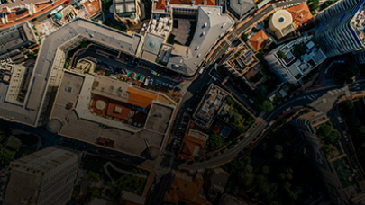 Aerial view of an urban area with buildings, streets, and some greenery. The image features a mix of high-rise and low-rise structures, with the central road network appearing to follow an organized agenda.