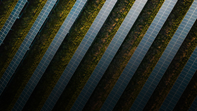 Aerial view of multiple solar panels arranged in parallel rows on a grassy field, seamlessly aligning with nature's agenda to create a pattern of alternating panels and greenery.