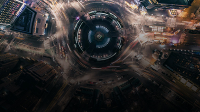 Aerial view of a city at night featuring a circular traffic roundabout in the center, surrounded by illuminated buildings and streets, all bustling with activity as if following an intricate agenda.
