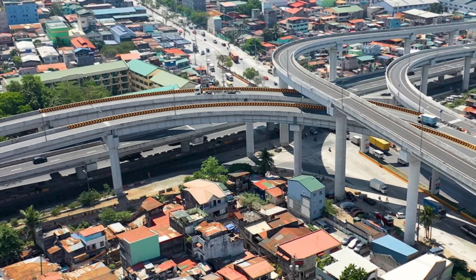 Aerial view of elevated highways and overpasses, including the NLEX-SLEX Connector Road, crossing above a residential area with houses and streets below—ideal for showcasing digital twin implementation in a major road project.
