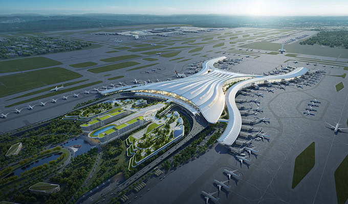 Aerial view of a large, modern airport terminal with multiple runways, taxiways, and airplanes parked at gates. The terminal features a distinctive, flowing architectural design.