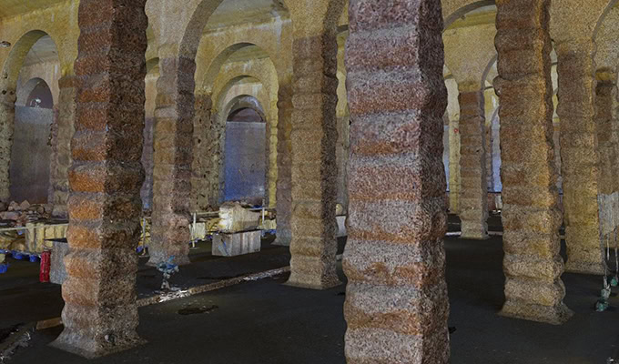 Stone columns with a textured, segmented surface stand in rows inside the dim, arched Ex-Sham Shui Po Service Reservoir chamber, where scattered debris covers the floor.