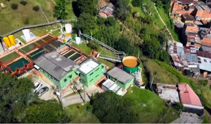 A water treatment facility, part of the Medellín Aqueduct Primary Network, is surrounded by greenery and residential buildings, viewed from above—a testament to advanced modeling and optimization in urban infrastructure.