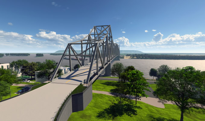 A steel truss bridge crosses the Mississippi River near Lansing, with green trees and grassy areas in the foreground beneath a partly cloudy sky.