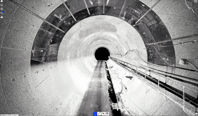 A grayscale image of a large, empty tunnel with cables and pipes running along the right wall, highlighting how digital technologies aid in infrastructure management, viewed from inside looking toward a dark circular opening.