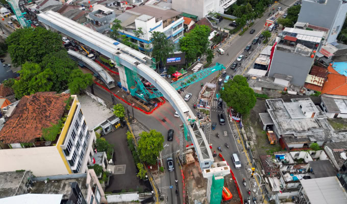 Aerial view of an urban construction site where Smart Infrastructure supports an elevated rail or bridge being built over a busy street, surrounded by buildings and traffic.