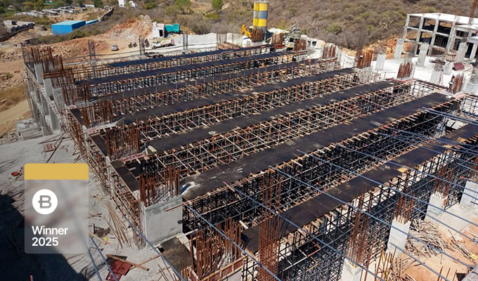 A construction site with reinforced concrete beams and columns being built for a power transmission project; a “Winner 2025” badge appears in the lower left corner.