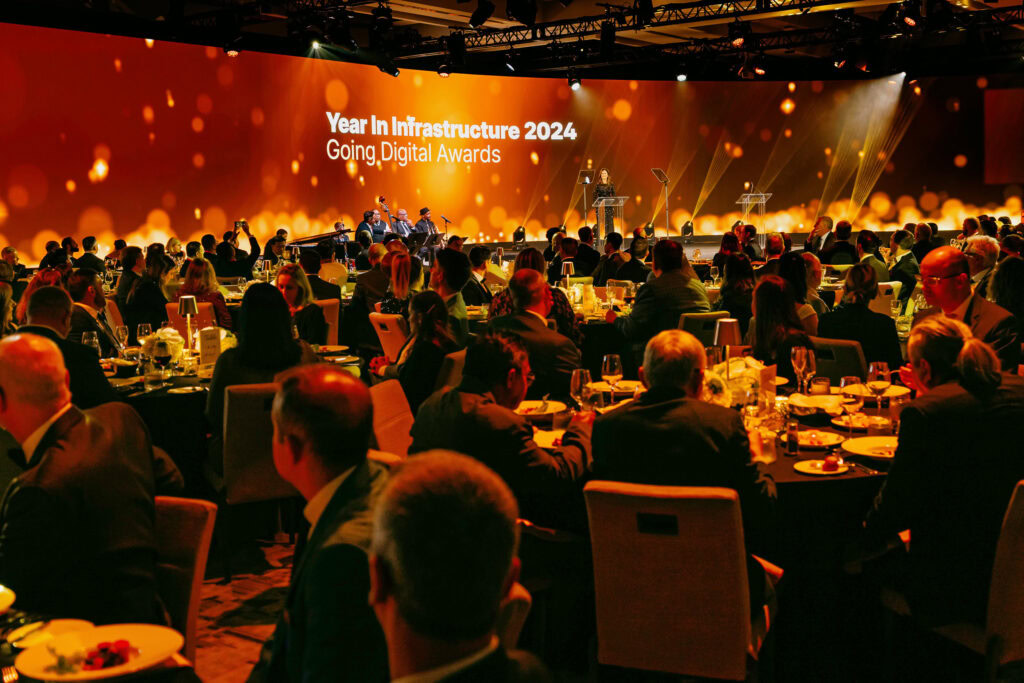 Guests seated at round tables attend the "Year in Infrastructure 2024 Going Digital Awards" event in a dimly lit venue with a large illuminated stage in the background.