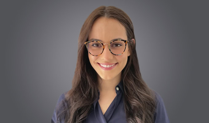 Marion Bouillin, a woman with long brown hair and glasses, smiles at the camera. She is wearing a dark collared shirt and stands against a plain gray background.