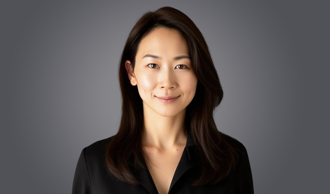 Yeun Jin Kim, a woman with straight dark hair wearing a black top, is looking at the camera and smiling slightly against a neutral gray background.