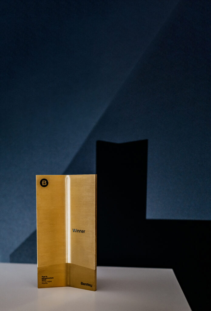 A gold Bentley award trophy labeled "Winner" stands on a white surface against a dark blue background with geometric shadows.