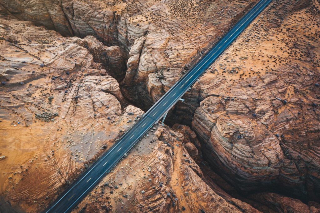 Aerial view of a straight road bridge crossing a deep rocky canyon in a desert landscape.
